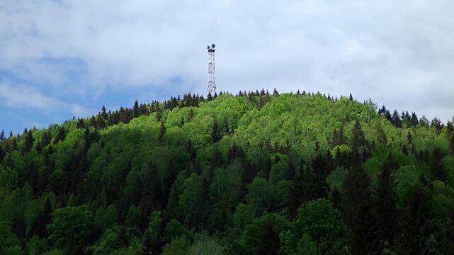 Distant view of 75m telecommunication radar tower on top of green mountain peak