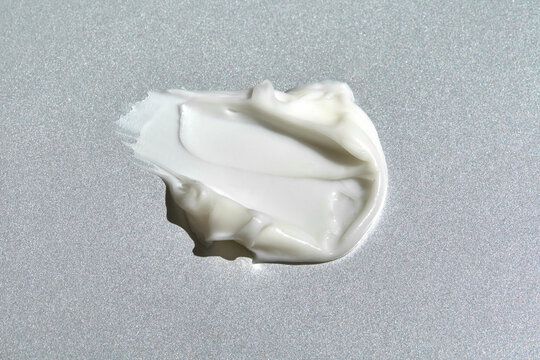 White cosmetic cream smear texture on silver background close up