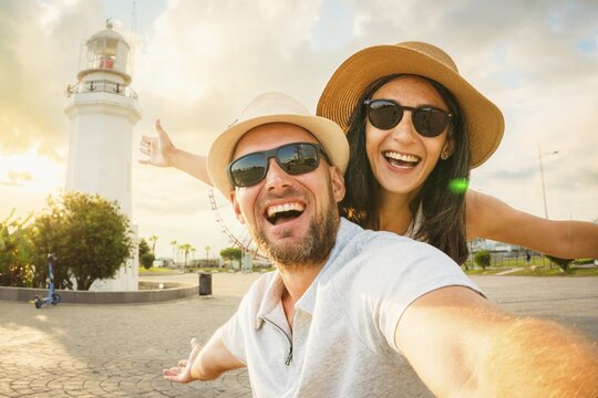 Young excited caucasian couple in love smiling taking selfie pov at Batumi Boulevard with iconic lighthouse and Ferris wheel during golden hour. Happy couple Holiday taking photo by popular landmarks