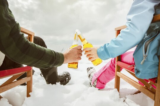 Couple relax sit on chairs in snowy ski resort with beer bottle, concept of leisure, winter holiday, relaxation, carefree lifestyle, freedom, cozy outdoor relaxation moment