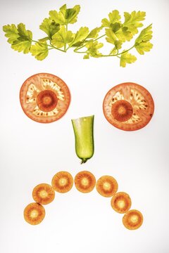 Sad face of vegetables, smiley face, slices of cucumber, carrot and tomato with parsley, white background, food photography