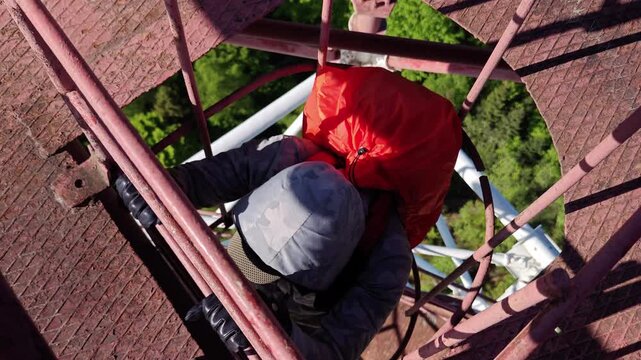 Man climbing vertical cage ladder inside 75m repurposed radar tower