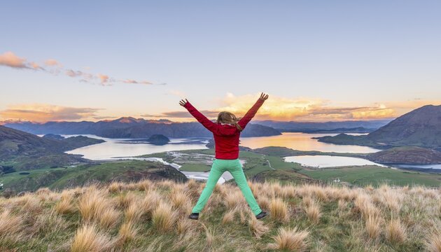 Hiker jumping with limbs spread out in the air, view of Lake Wanaka and mountains, sunset, Rocky Peak, Glendhu Bay, Otago, Southland, New Zealand