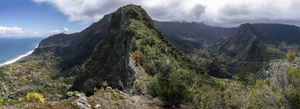 Hikers on the ridge of Pico do Alto, panorama, view of densely overgrown mountains and the village of Boaventura, view of the coast and sea with the village of Arco de Sao Jorge, Madeira, Portugal