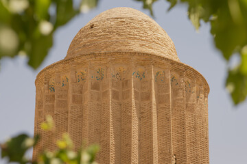A close-up telephoto shot showcasing the upper section, cornice details, and dome of the historic Kashaneh Tower (Kashane Tower) in Bastam, Semnan Province, Iran.  © Contentino