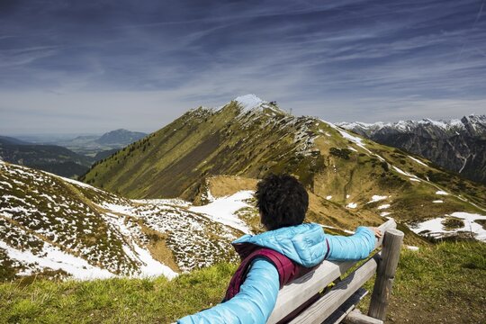Woman, 50-55, sitting relaxed on a bench, sunbathing, behind her the Fellhorn, near Oberstdorf, Allg&auml;u, Bavaria, Germany