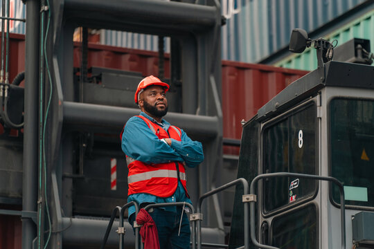 Port worker in hard hat and safety vest beside cargo crane at shipping terminal, confident industrial scene