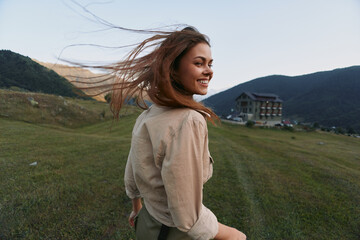Fototapeta premium Smiling woman outdoors in a field turns toward the camera with wind in her hair. Casual clothing, natural light, and open landscape convey a carefree lifestyle and joy.