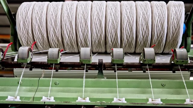 Yarns are transferred from bobbins into a machine line inside a textile factory. This video frame shows yarn flow, spinning process, machine detail, automation, and industrial production.