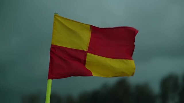 Low-angle shot of a vibrant yellow and red checkered fan flag waving on a bamboo pole on an outdoor sports court during tournament celebrations in Dhaka, Bangladesh.