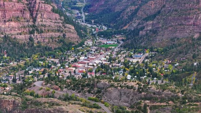 Aerial view of Ouray, Colorado town known as Switzerland of America in box canyon landscapes with mountainside cliffs and fall foliage tree during autumn season colors in San Juan Mountains - 4K Drone