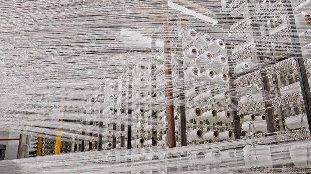 White warp yarns are transferred from bobbins into the production line inside a textile factory. This video frame shows weaving preparation, yarn tension, bobbin system, and industrial textile process