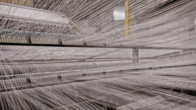 White warp yarns are transferred from bobbins into the production line inside a textile factory. This video frame shows weaving preparation, yarn tension, bobbin system, and industrial textile process