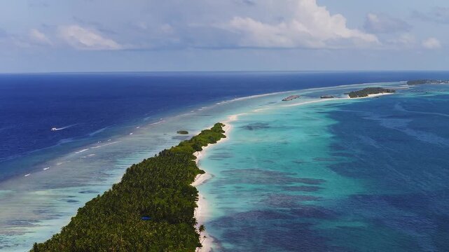 Aerial view of Dhigurah island, Maldives, with palm sandbank, white beaches, turquoise shallows, fringing reef, lagoon gradients, islets, over water structures, and a speedboat