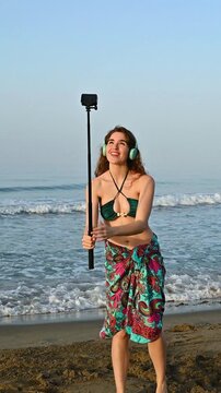 Young female influencer vlogger recording a selfie beach diary at sunrise, speaking to the camera, sharing holiday memories by the ocean, authentic summer storytelling, UGC creator