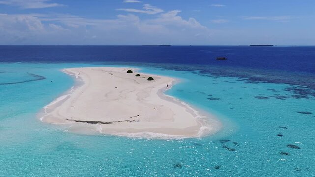 Aerial view of Dhigurah sandbar in Maldives, lone walker, swimmers, anchored dhoni, turquoise to indigo lagoon, shrubs, coral patches, gentle waves at midday