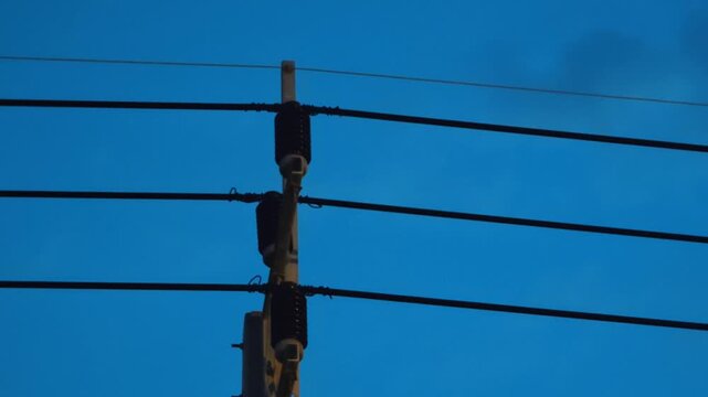 Partial discharge spark on high voltage overhead power line cover tie wire on utility pole against dark blue evening sky. Electrical fault and grid maintenance concept.