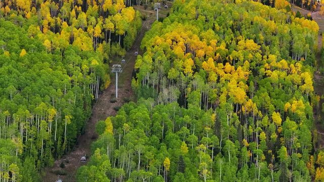 Aerial view of gondola in Telluride, Colorado mountain ski town among fall foliage trees along mountainside in San Juan Mountains landscape during autumn season - 4K Drone