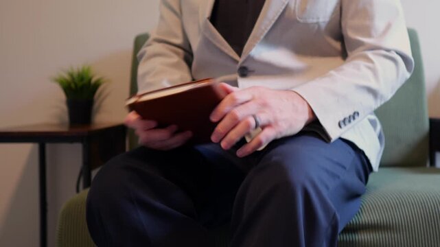Middle aged candidate anxiously reviews handwritten notes in a leather notebook while waiting for a corporate business job interview in stale office