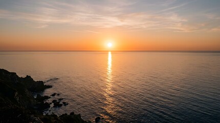 Obraz premium Vibrant sunset painting the sky and sea with warm golden light above a rocky shore
