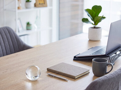Clean and minimalist home office desk featuring a clear glass sphere, a notebook, a pen, a coffee mug, and a laptop.