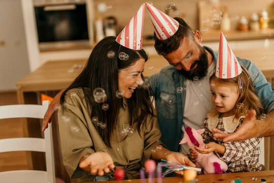 Family celebrating daughter's birthday with bubbles and party hats
