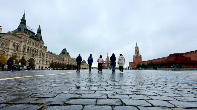 Tourists walking on cobblestone square near historic landmark. People travel in urban city center. Old architecture and tower in background. Travel trip landscape.
