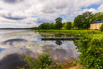 Fototapeta premium Beautiful view of lakeside pier with reflections and historic manor beside tranquil water. Sweden.