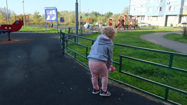 Little female child playing with soap bubbles at urban playground. Happy kid blowing bubbles in city park courtyard. Childhood activity, leisure and fun playtime.
