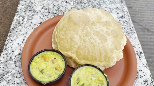 Slow push-in 4K footage of golden puffed puri served with creamy Indian vegetable curry in small bowls on a red plate, showcasing a traditional breakfast with rich texture and vibrant colors.