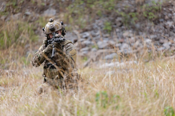 Fototapeta premium Soldier in military gear aims weapon while crouching in tall grass
