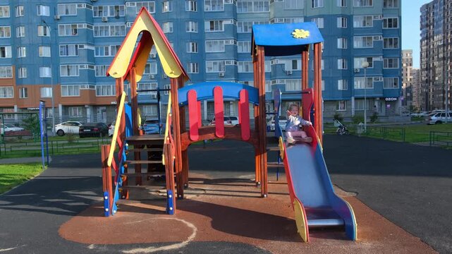 Little toddler girl sliding down a slide at the playground. Childhood recreation in urban courtyard. Happy female child playing on outdoor equipment in city area.