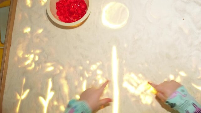 A toddler plays in a sand table with decorative crystal gems. Child engages in sensory play activity on a light box surface for fun education and development.