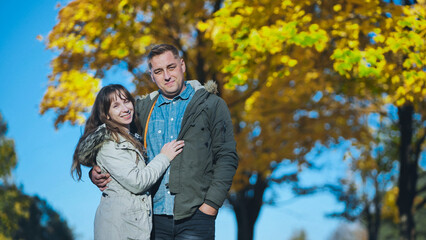 Fototapeta premium Romantic couple enjoying a sunny autumn day in a park with colorful foliage, embracing and smiling