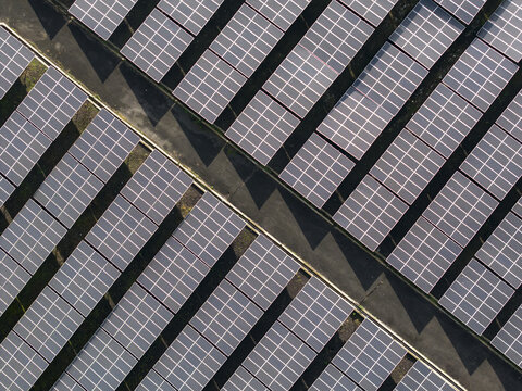 Aerial view of PLTS 1MWp Bangli solar farm with rows of photovoltaic panels arranged in a geometric pattern separated by a maintenance path in Bangli, Bali, Indonesia.