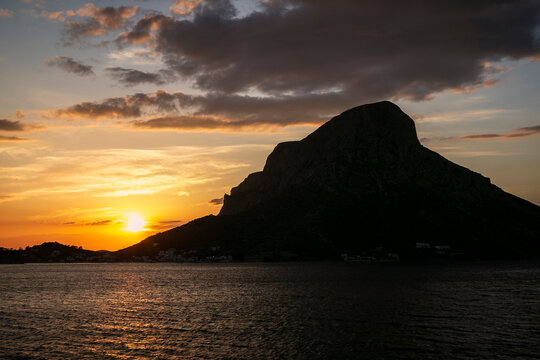 Scenic view of orange sky, the village and silhouette of the steep Telendos island in Greece at sunset.