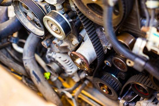 An extreme close-up of a car engine block with a black toothed timing belt and metal pulleys. automotive repair parts, vehicle motor.