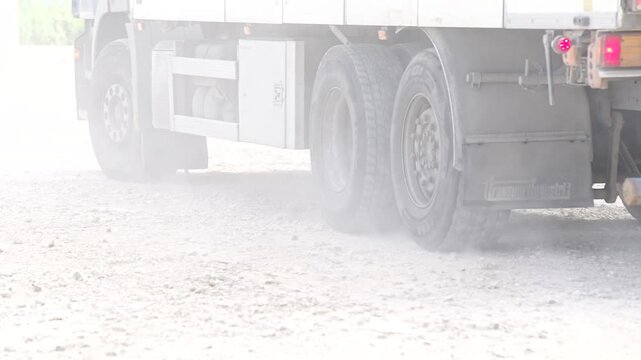 Heavy duty dump truck tires rotating on a loose gravel surface while kicking up a plume of dust during industrial material transportation at a work site