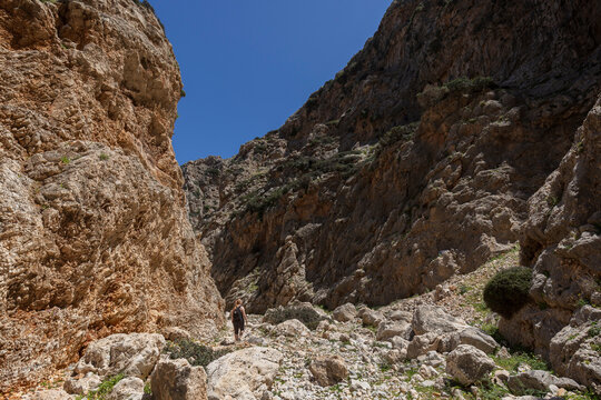 A woman hiking at the stunning Katholiko (or Avlaki) Gorge which features tall, steep, rugged and rocky cliffs, on a sunny day in Crete, Greece.