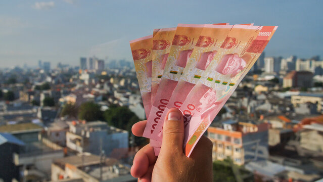 Man's Hand holding rupiah money against the backdrop of the city of Jakarta.