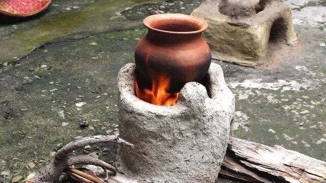 clay pot placed over a wood-fired clay stove (chulha) with a natural fire burning underneath in a rural village setting.  Chhath Kheer or Pongal making using age old methods