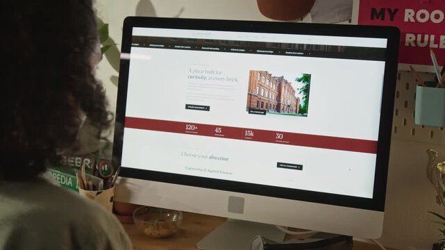 Over-the-shoulder shot of unrecognizable teenager scrolling university website on computer and celebrating college acceptance letter. For higher education marketing and student recruitment campaigns