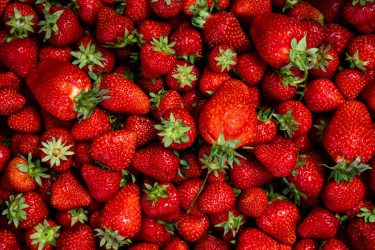 Full frame view of fresh ripe red strawberries with green leaves background texture
