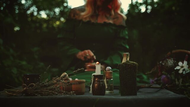 Unrecognizable person gothic blurred silhouette woman preparing healing potion medicine at wooden table with food drink in dusk mystery night forest trees. glass bottles candles light close-up detail