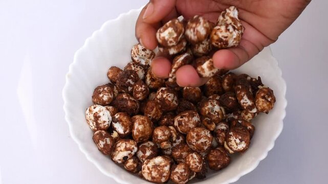 hand picking jaggery and cocoa-coated makhana (fox nuts) from a white bowl, nutrients rich and makes an ideal guilt-free option for weight loss. 