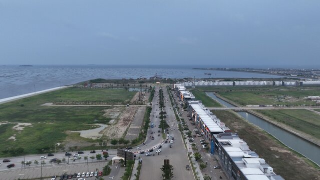 Aerial view of PIK 2 development featuring modern commercial buildings, a coastal road with traffic, and open green spaces along the Java Sea in Kosambi, Banten, Indonesia.