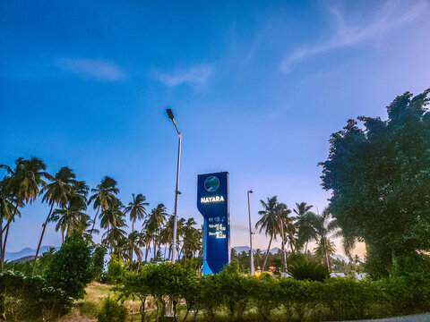 Theni, Tamil Nadu, India &ndash; June 27, 2026: Nayara Energy fuel station sign stands amid coconut palms under dramatic evening clouds, with the Western Ghats forming a scenic backdrop in Theni district