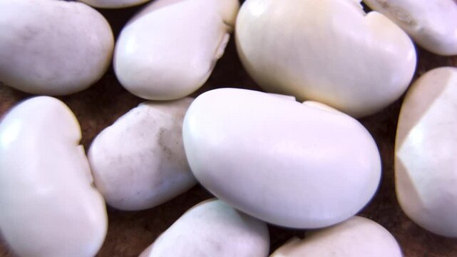 Extreme macro close up of raw white kidney beans Phaseolus vulgaris rotating on wooden texture background, showcasing organic food ingredient