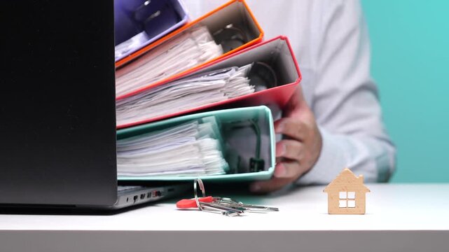 Person holding a stack of colorful file binders filled with documents. Symbolizing extensive paperwork and bureaucracy involved in real estate transactions