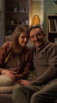 Vertical portrait shot of Caucasian adult woman and middle aged man sitting on sofa, smiling at camera. Footage suitable for family counseling, real estate, or home insurance campaigns